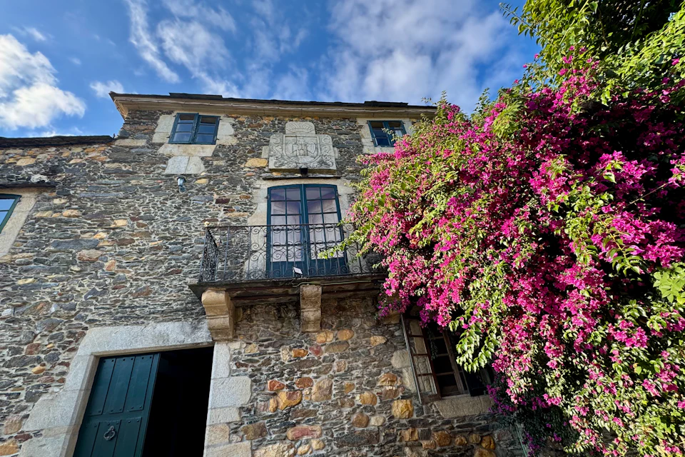 Casa de piedra cun balcón y buganvilla en flor